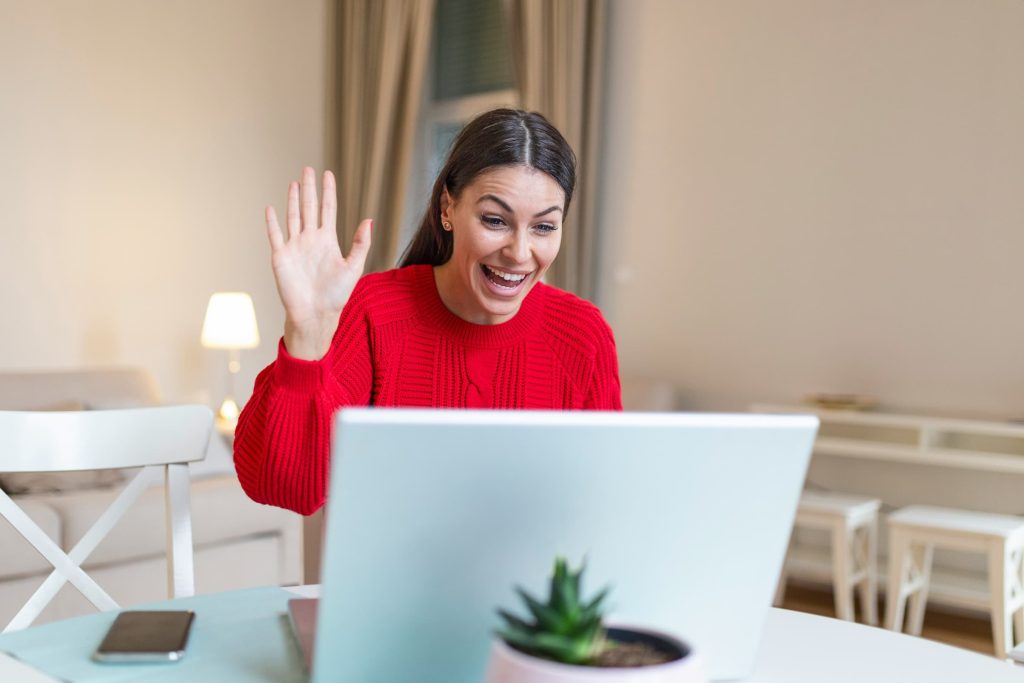 a woman on a virtual job interview smiling and waving to her computer