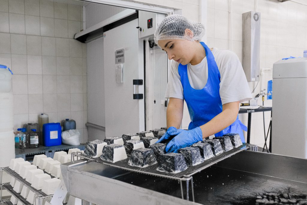 Woman with a Blue Apron and Gloves Producing White Cheese in a Factory
