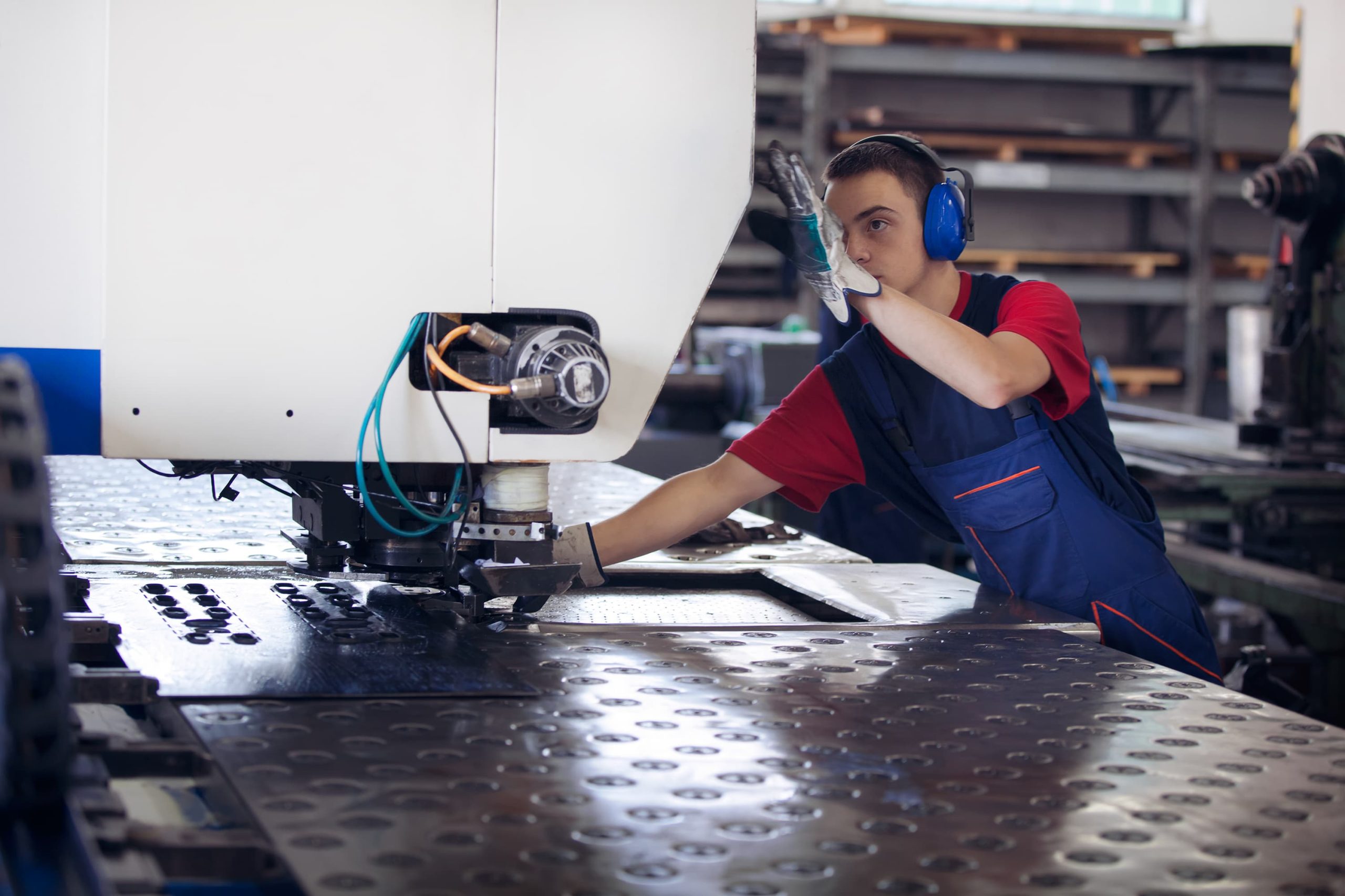 Inside a factory, industrial worker in action on metal press machine holding a steel piece ready to be worked.